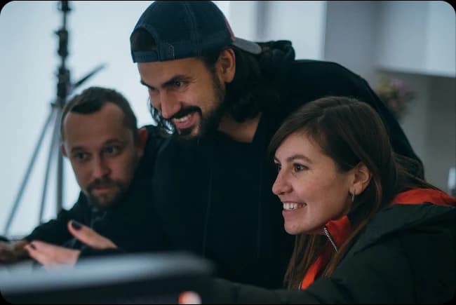 Three members of a production team leaning in to review work on a screen together.