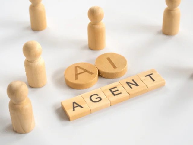 Wooden figures scattered on a white surface beside tiles spelling AI agent