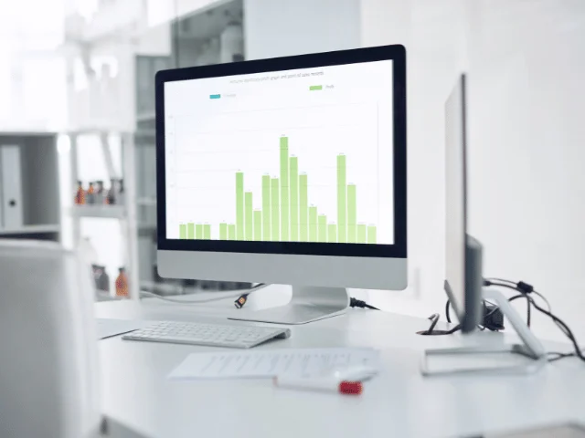 A desktop monitor on a white desk showing a green bar chart