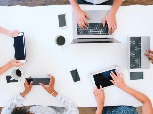 Overhead view of a table where several people use laptops, tablets and phones