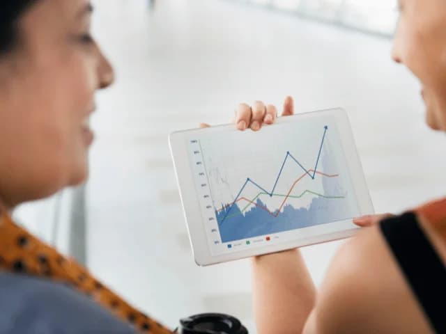 Two colleagues smiling at a tablet that shows a multi-line performance chart