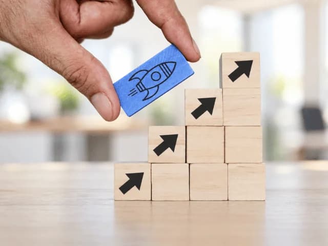 A hand placing a blue rocket block on a staircase of wooden blocks marked with upward arrows