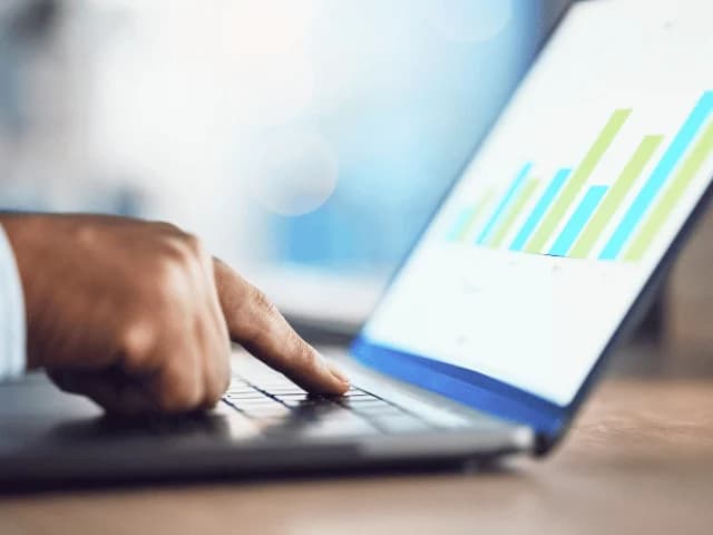 A hand on a laptop keyboard, the screen showing a green and blue bar chart