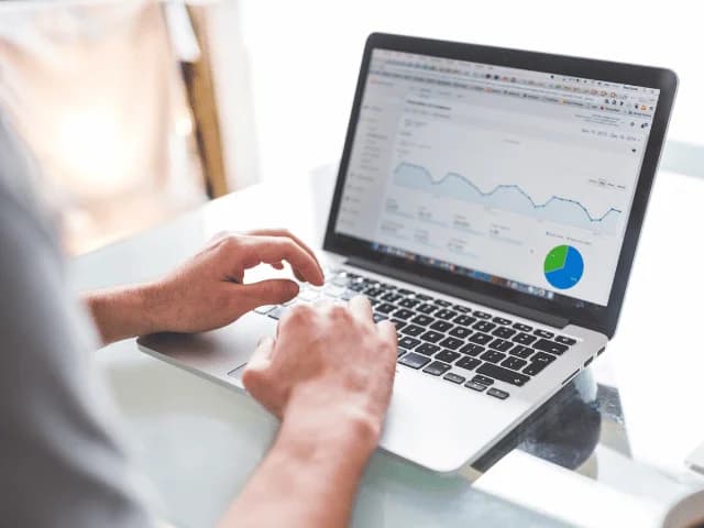 Hands on a laptop keyboard, the screen showing an analytics dashboard with a line chart and a pie chart