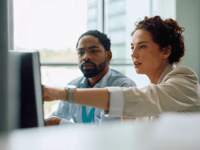 A man and a woman looking at a monitor, the woman pointing at the screen