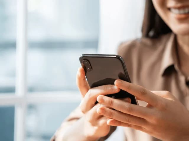 A smiling woman using a phone held in both hands