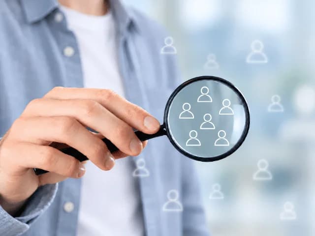 A hand holding a magnifying glass over a cluster of person icons