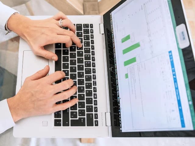 Overhead view of hands typing on a laptop with a green bar chart on the screen