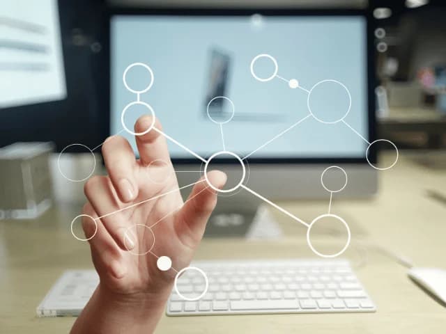 A hand reaching toward a diagram of connected circles, with a monitor and keyboard behind it