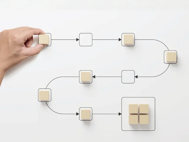 A hand placing a wooden block onto a flowchart of boxes and arrows on a white surface